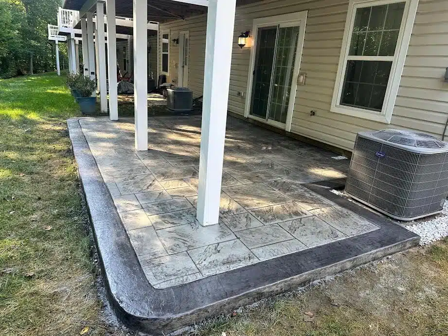 Concrete patio with a dark contrasting border beside a home with white pillars