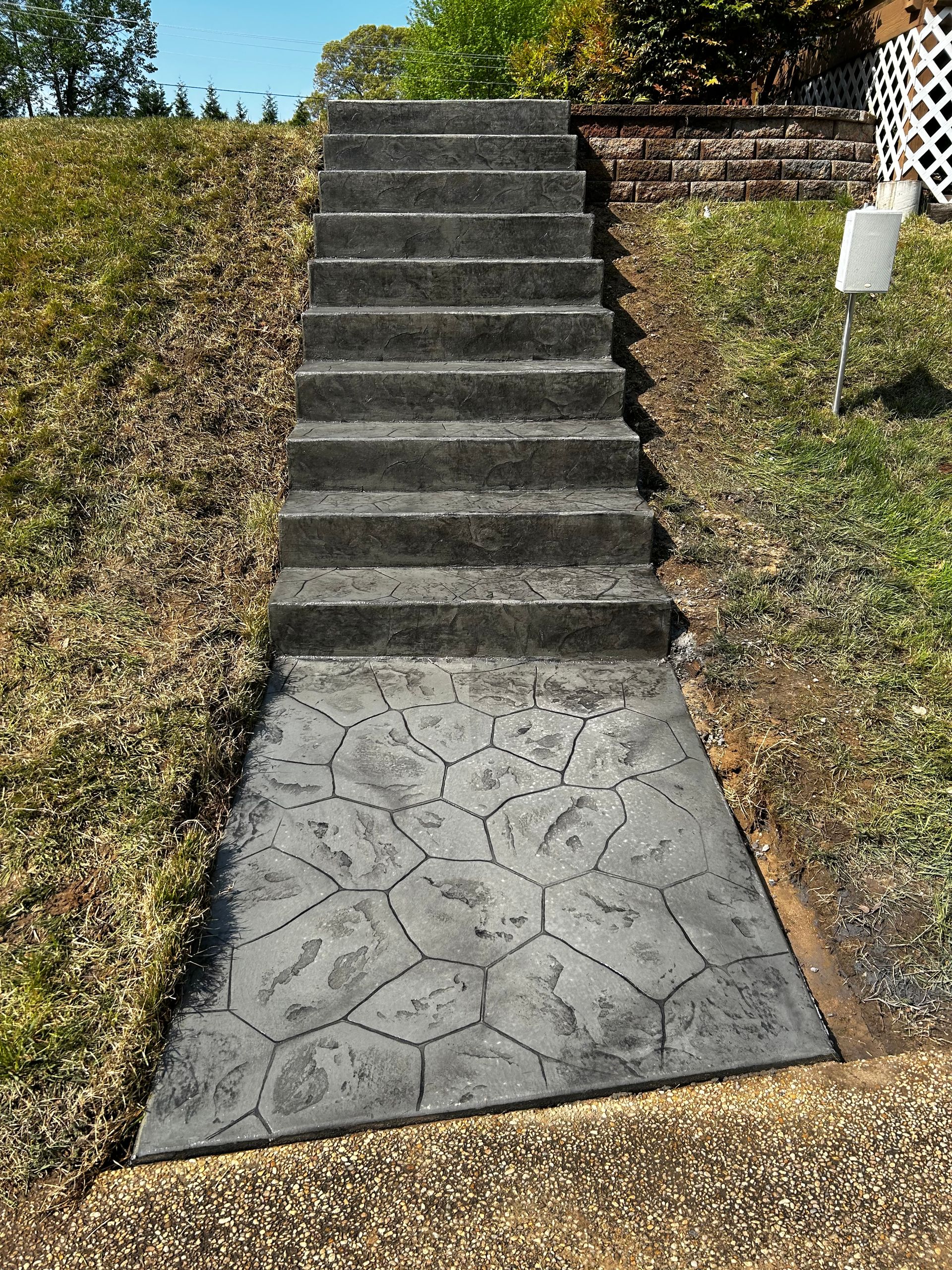Concrete steps leading up a grassy hill, with a patterned walkway at the base.
