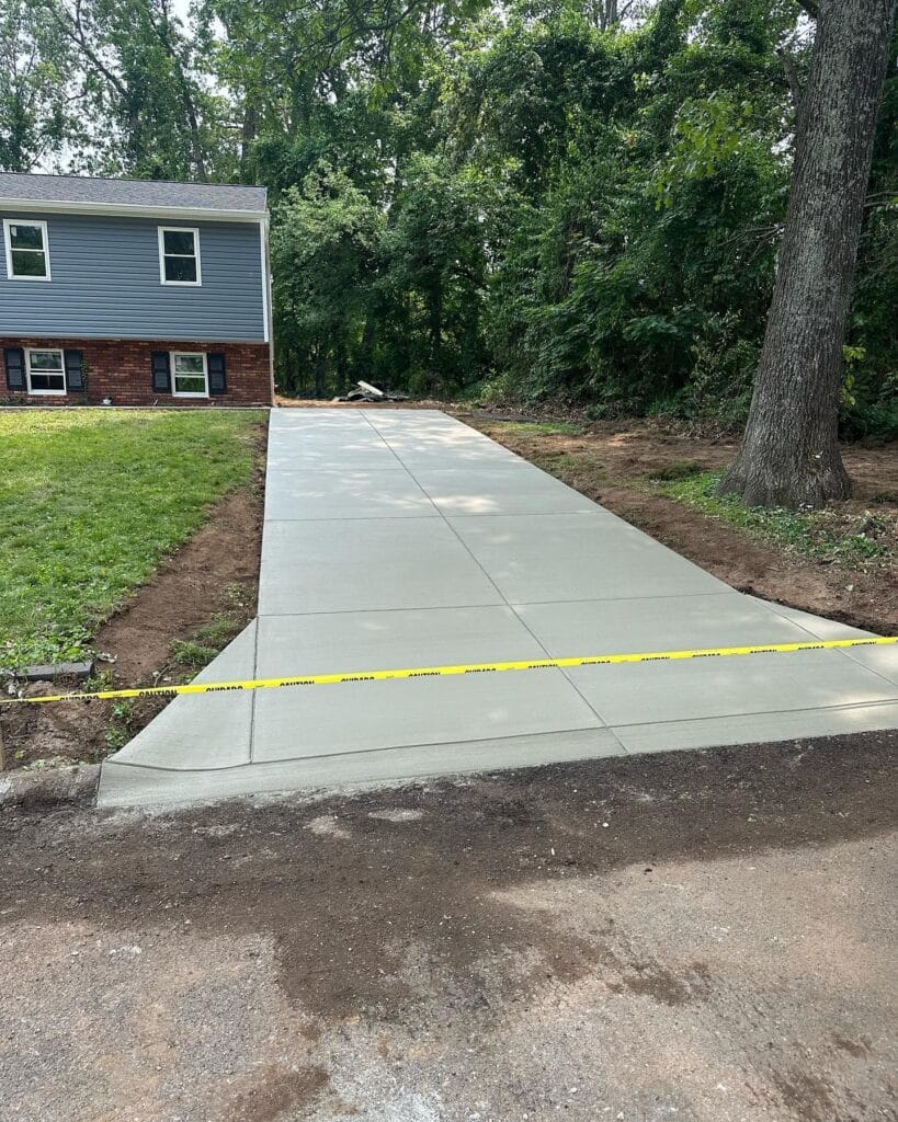 New concrete driveway leading to a two story house with blue siding