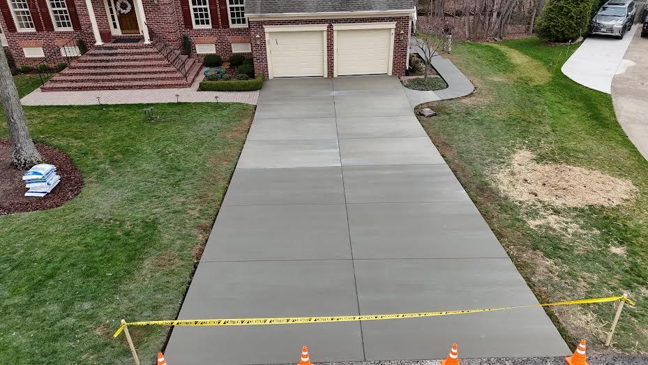 Newly poured concrete driveway with caution tape in front of a brick home
