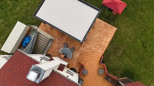 Overhead view of a house with a multi-level wooden deck, metal pergola, and red roof
