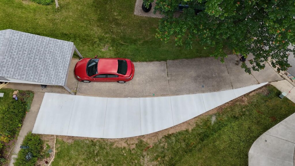 Overhead view of a car parked on a gray concrete driveway beside a garage