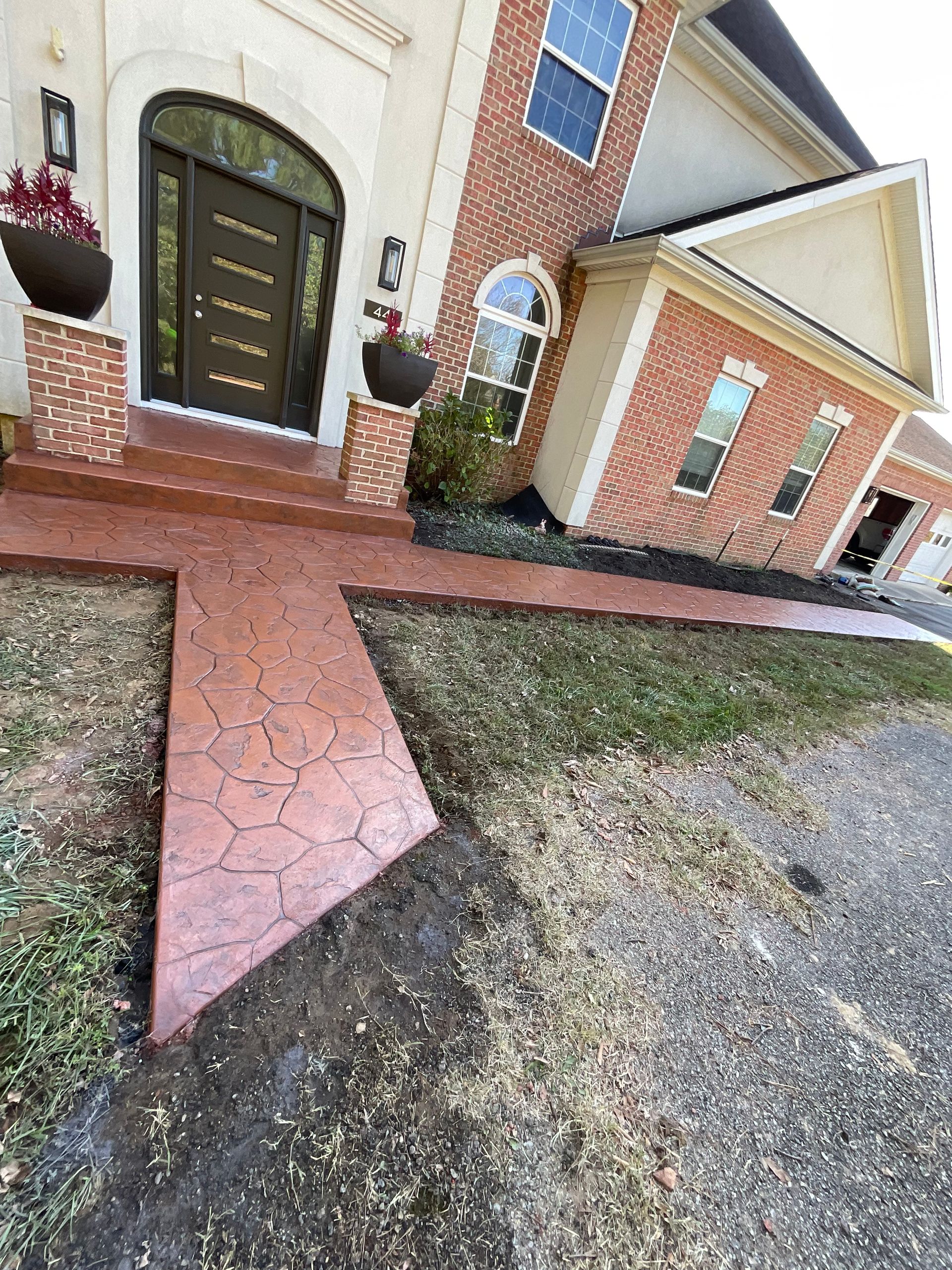 Stamped concrete walkway leading to a brick home's entryway. Red-brown colored concrete.