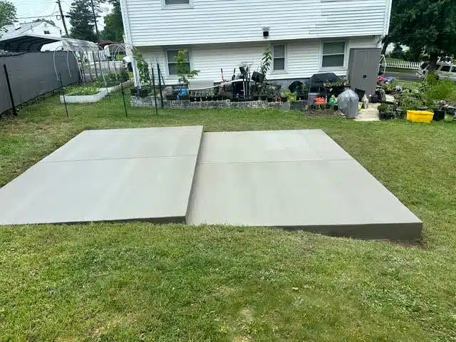 Two adjacent gray concrete pads forming a patio area in a grassy backyard