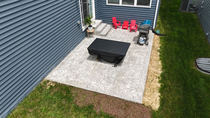 Freshly poured concrete driveway in front of a two-story brick house, caution tape, blue sky.