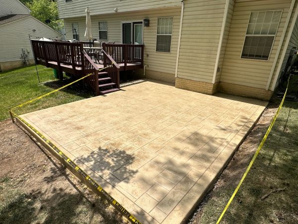 Newly constructed outdoor patio adjacent to a house with a wooden deck. Yellow caution tape surrounds the patio.
